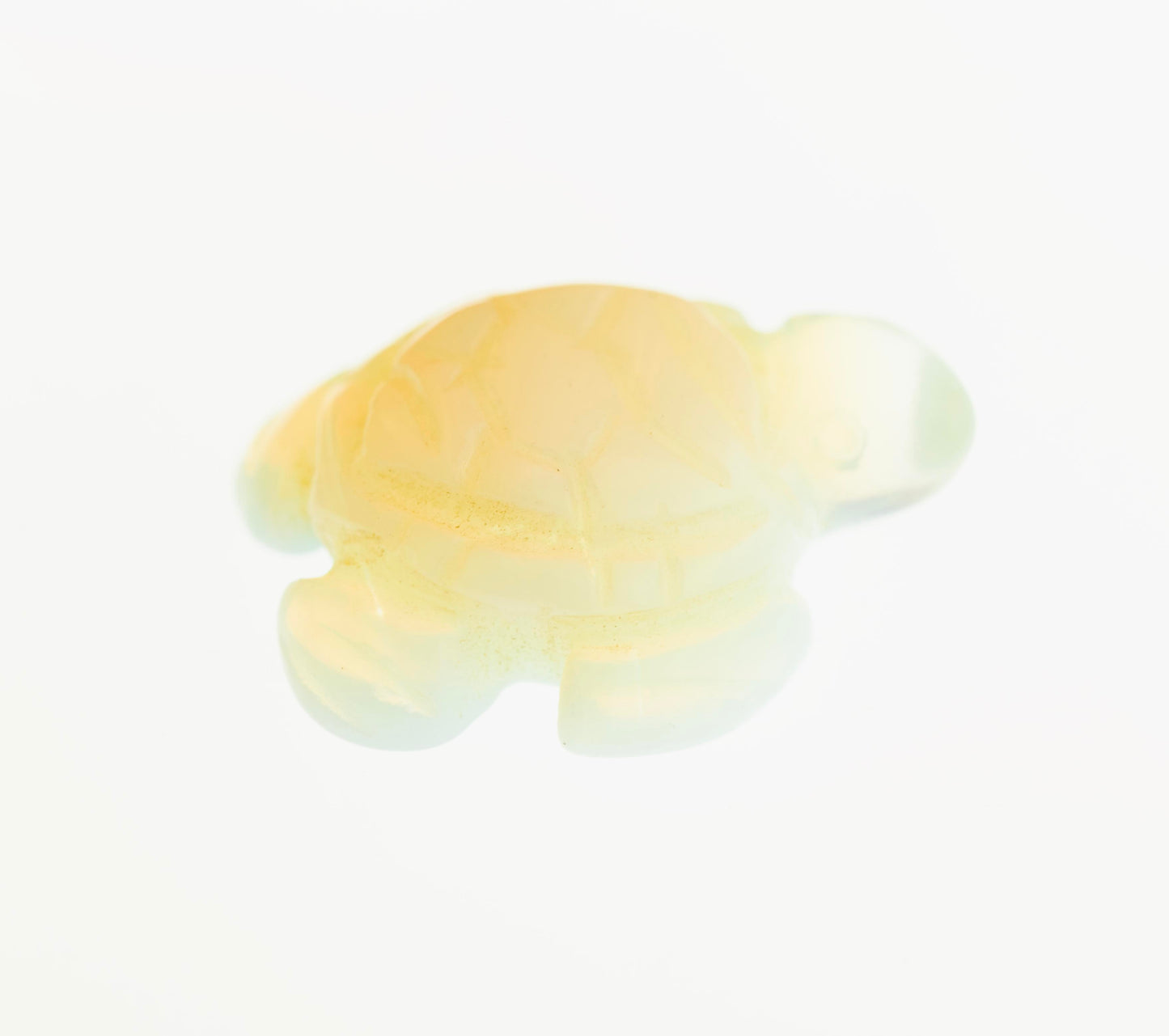 Close-up of a small, light-yellow, translucent plastic or resin turtle figurine on a white background, reminiscent of delicate Carved Turtle Gemstone Figures crafted from Aventurine.
