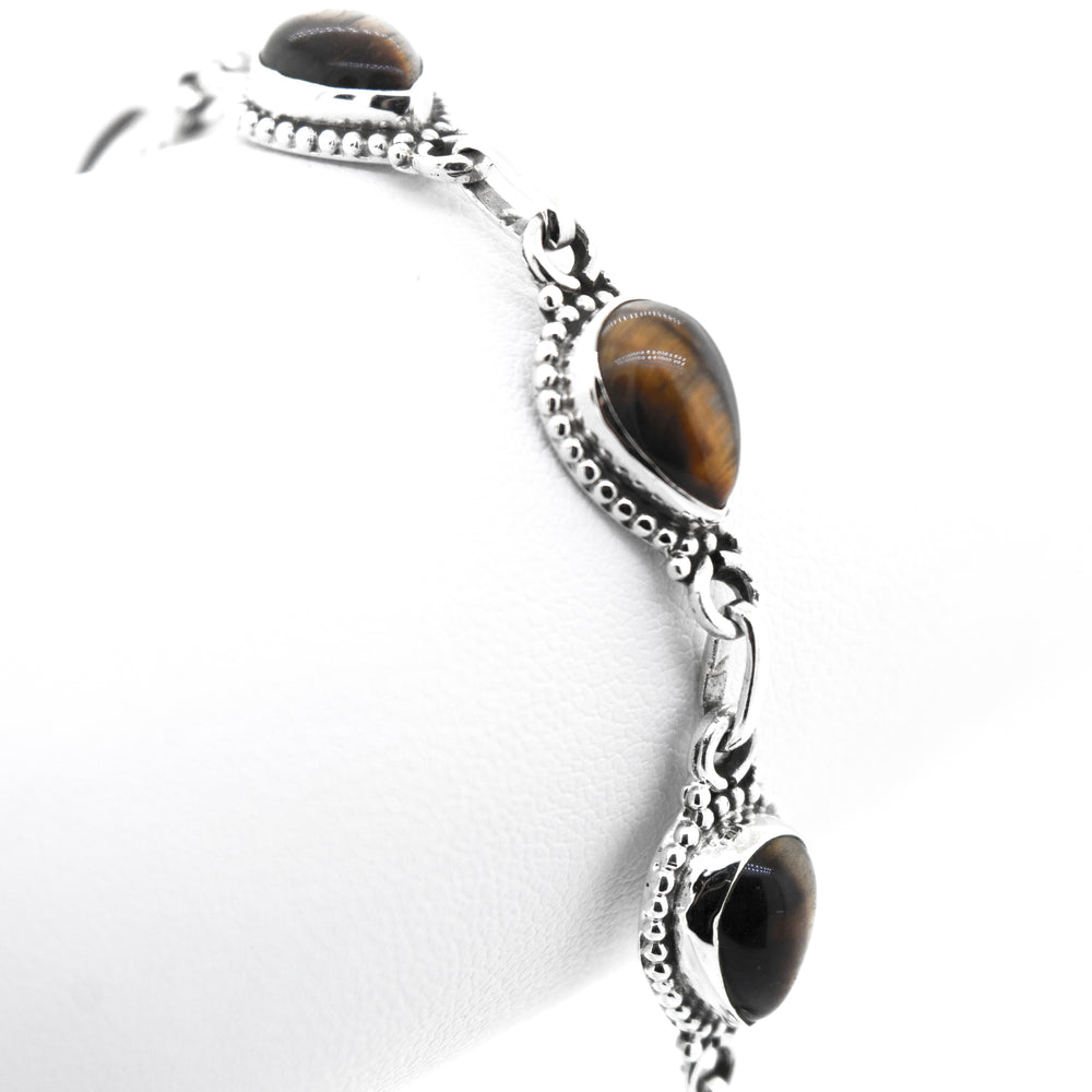 
                  
                    A close-up of a stunning Teardrop Shape Stone Bracelet With Ball Border featuring three tiger's eye gemstone settings on a plain white background.
                  
                