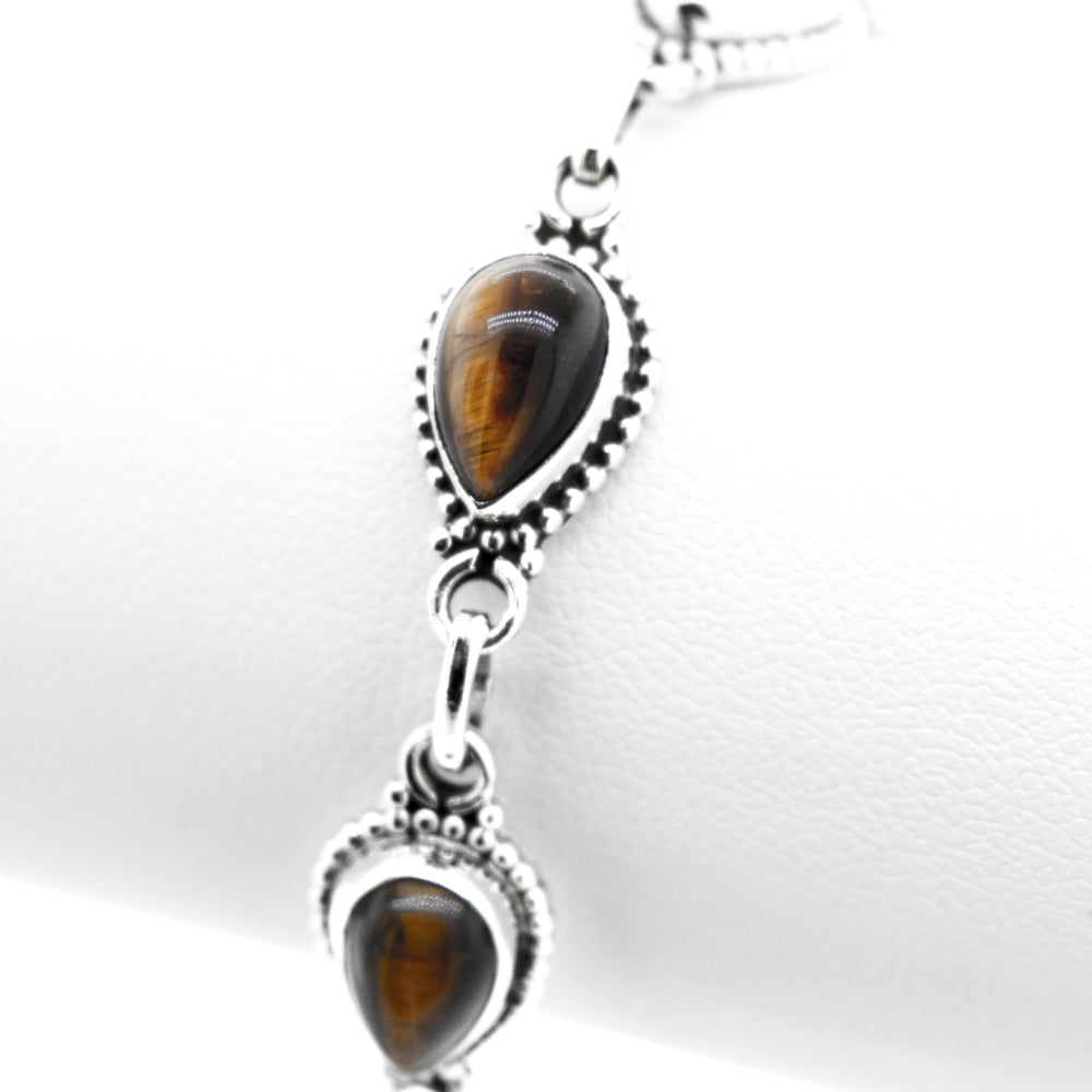 
                  
                    A Teardrop Shape Stone Bracelet With Ball Border featuring tear-shaped tiger's eye gemstones set in .925 silver, attached with circular links, displayed on a white background.
                  
                
