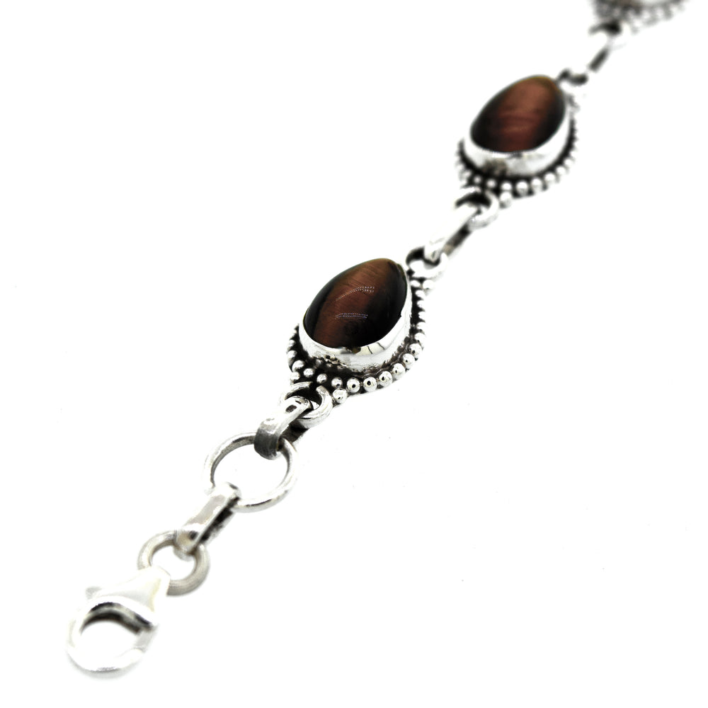 
                  
                    A Teardrop Shape Stone Bracelet With Ball Border with two oval-shaped, brown Tiger's Eye gemstones in decorative settings, connected by small links and a lobster clasp.
                  
                