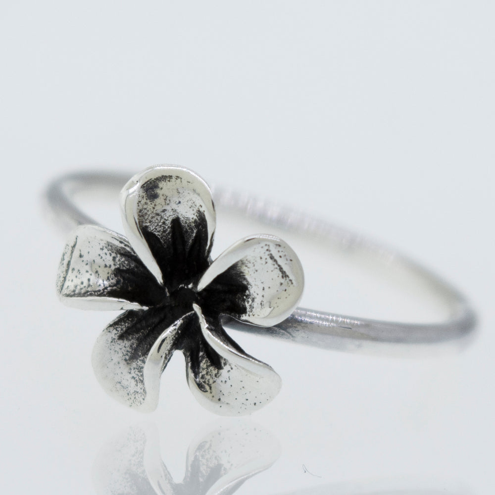 A Plumeria Ring featuring a black and white flower on a white surface.