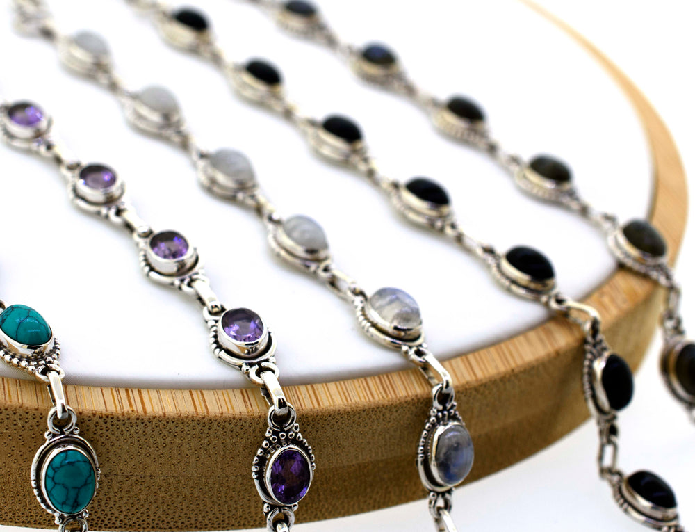 A group of oval gemstone bracelets with half ball border on a wooden stand by Super Silver.