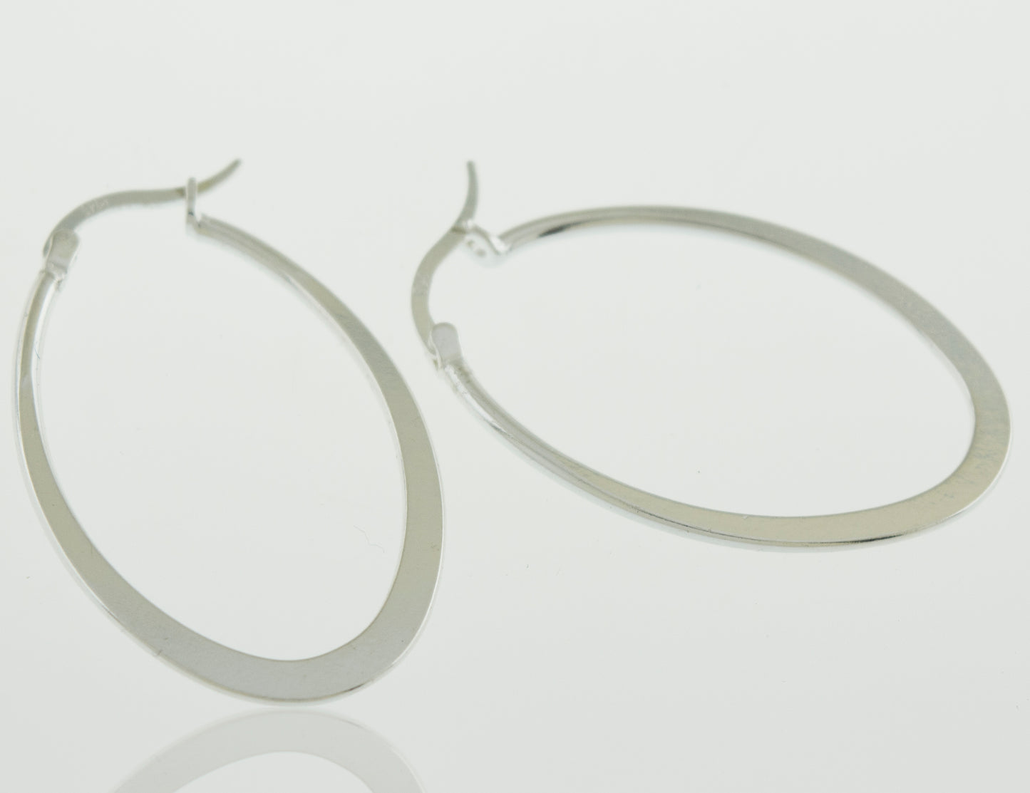 A pair of Super Silver Oval Shaped Hoop earrings on a white surface.