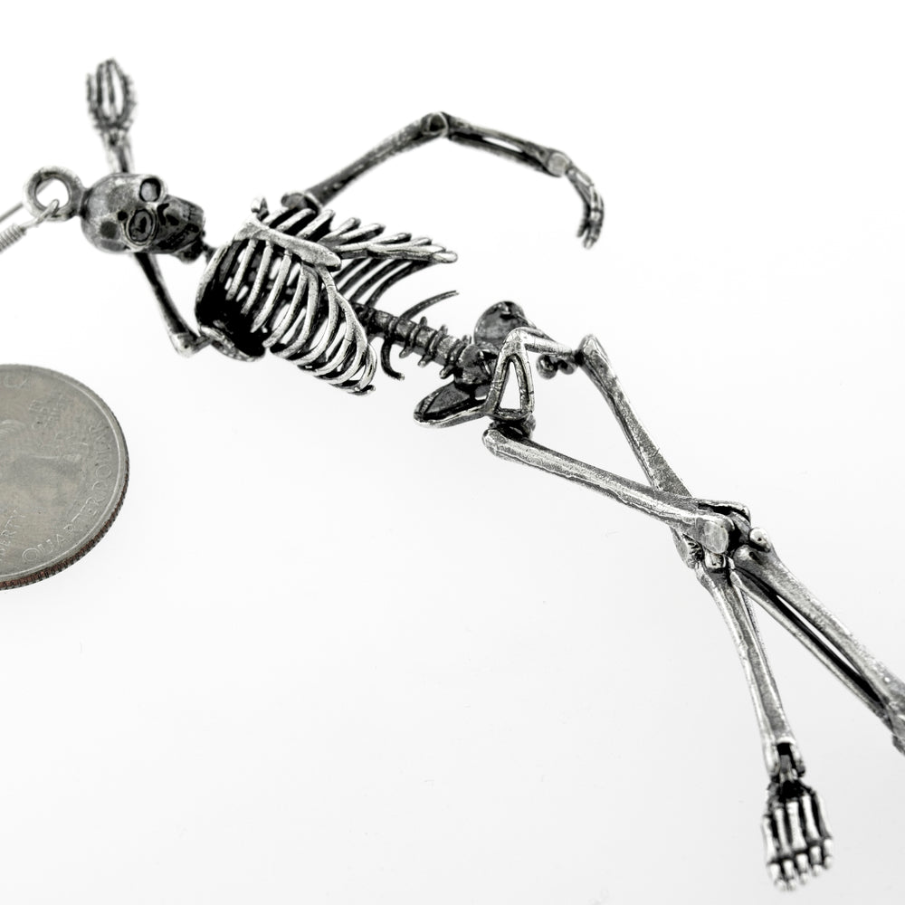 
                  
                    A spooky-themed Super Silver skeleton earring crafted in Sterling Silver, featuring a chilling design of a skeleton laying on top of a coin.
                  
                