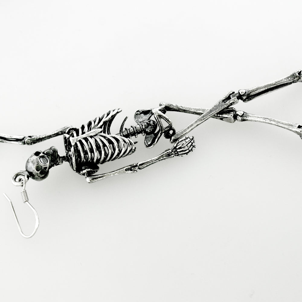 Spooky-themed Super Silver sterling silver skeleton earrings dangle from a chain on a white surface.