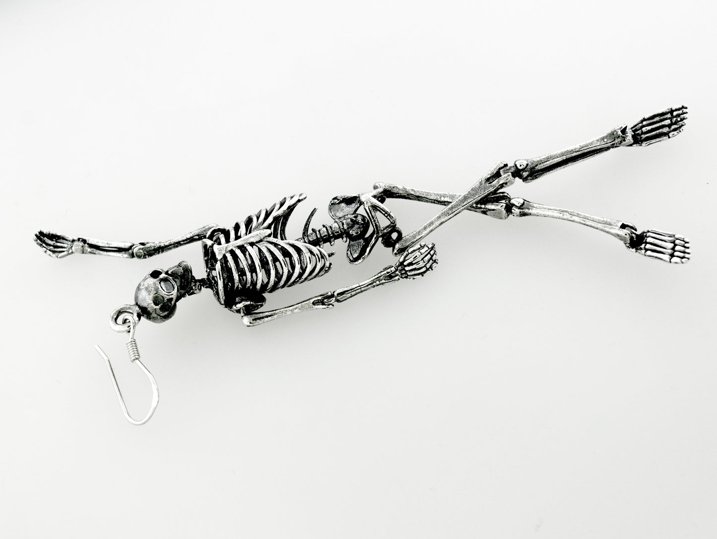 
                  
                    Spooky-themed Super Silver sterling silver skeleton earrings dangle from a chain on a white surface.
                  
                