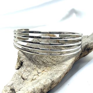 A Simple Cuff with Open Design made by Super Silver rests elegantly on a piece of driftwood.