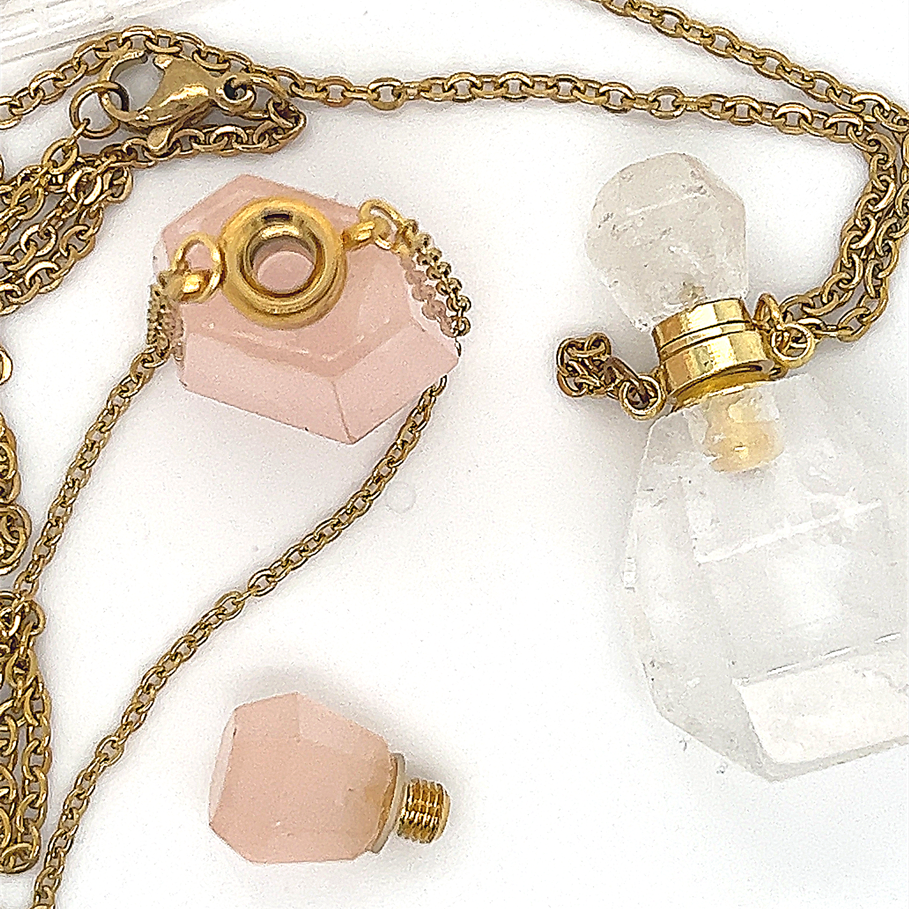 The Crystal Perfume Vial Necklace features a gold chain and a rose quartz pendant shaped like an essential oil vial with a detachable pink cap and gold accents, shown on a white surface.