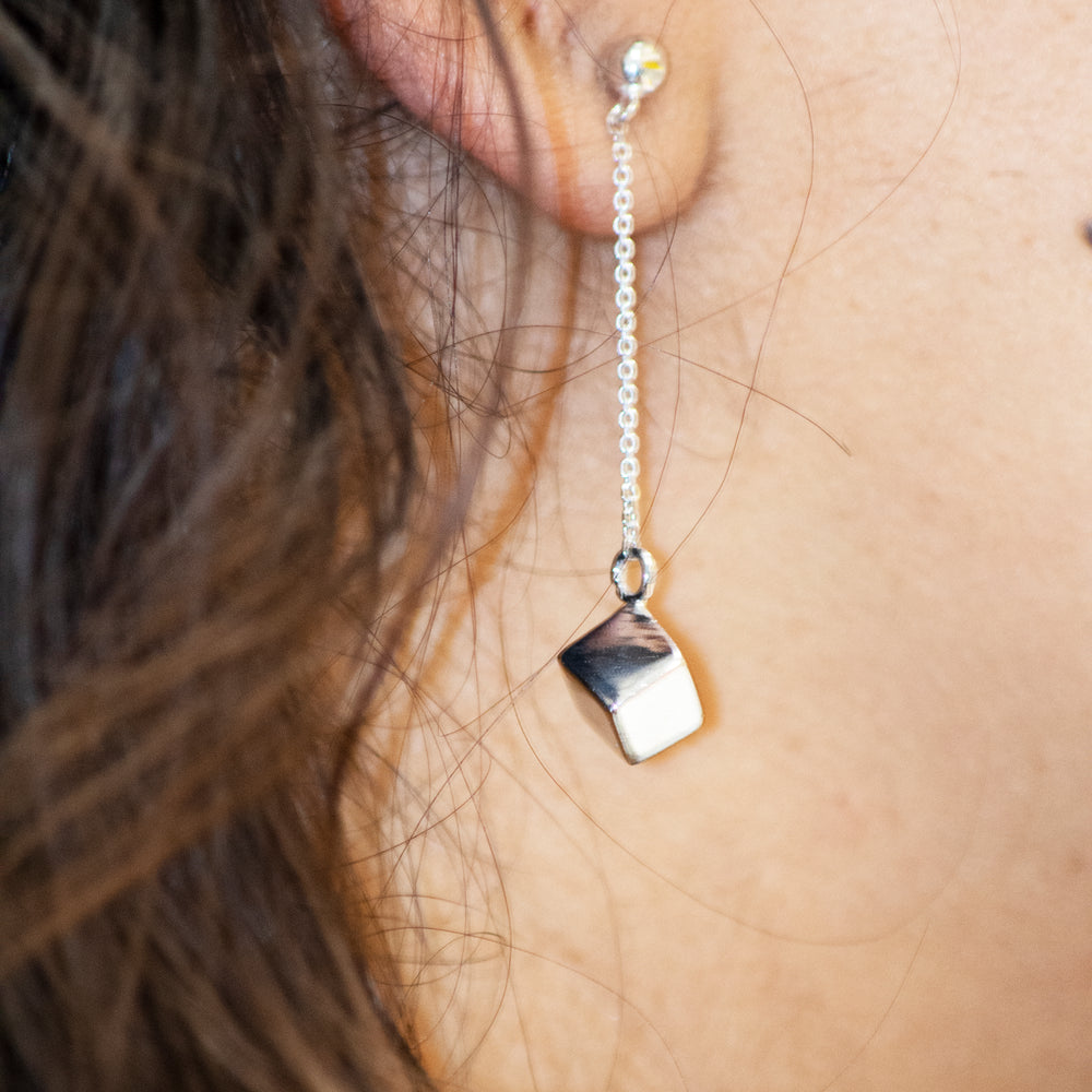 A close up of a woman's ear with Super Silver's Silver Drop Earrings with a Solid Cube.