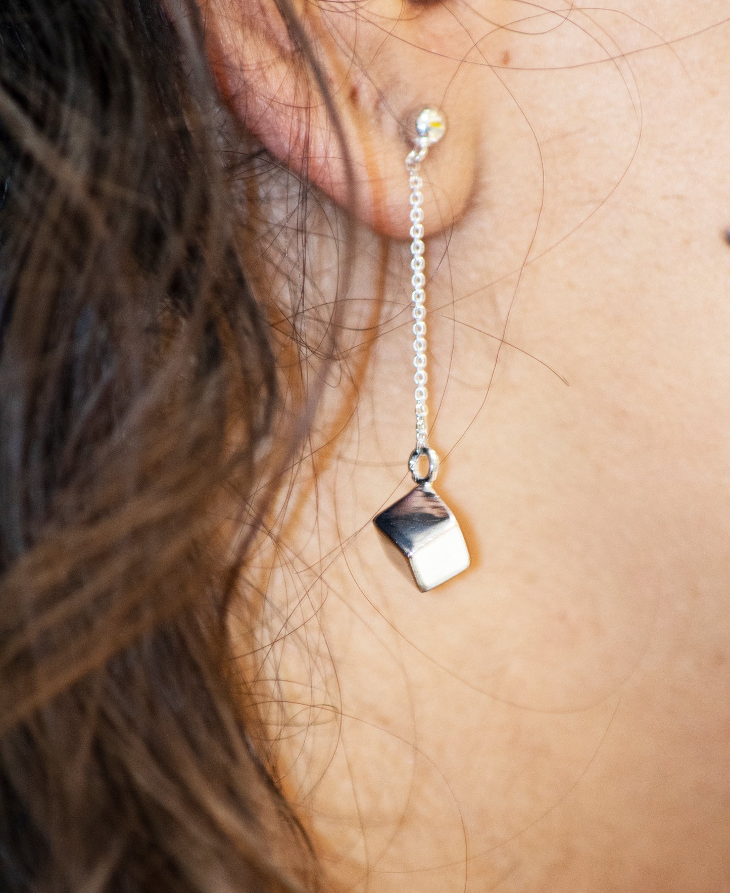 A close up of a woman's ear with Super Silver's Silver Drop Earrings with a Solid Cube.