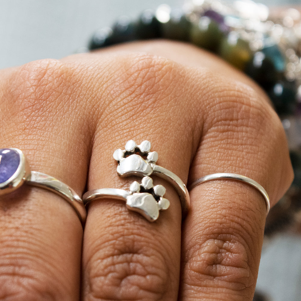 A woman's hand is holding a Super Silver Dog Paw Print Adjustable Ring.