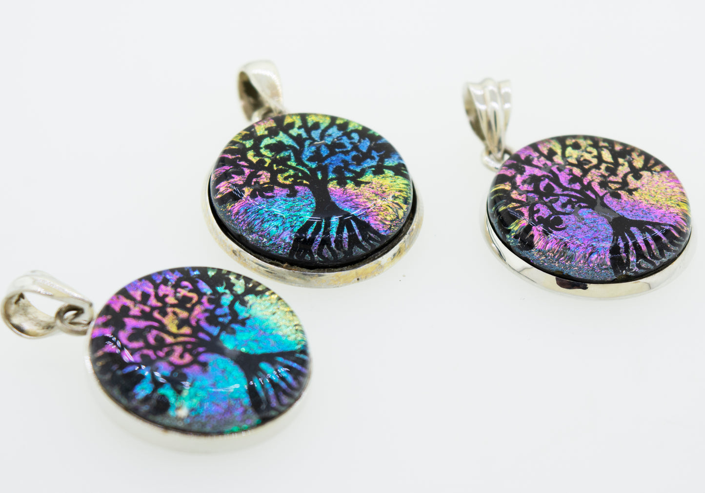 Three vibrant Super Silver Dichroic Glass Tree Of Life pendants on a white surface.