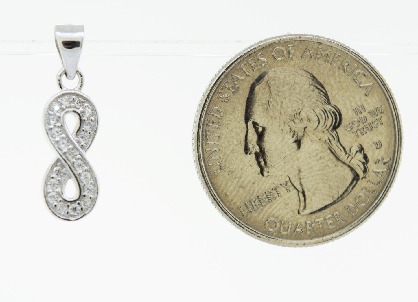 A Cubic Zirconia Infinity Pendant from Super Silver shimmering beside a penny.