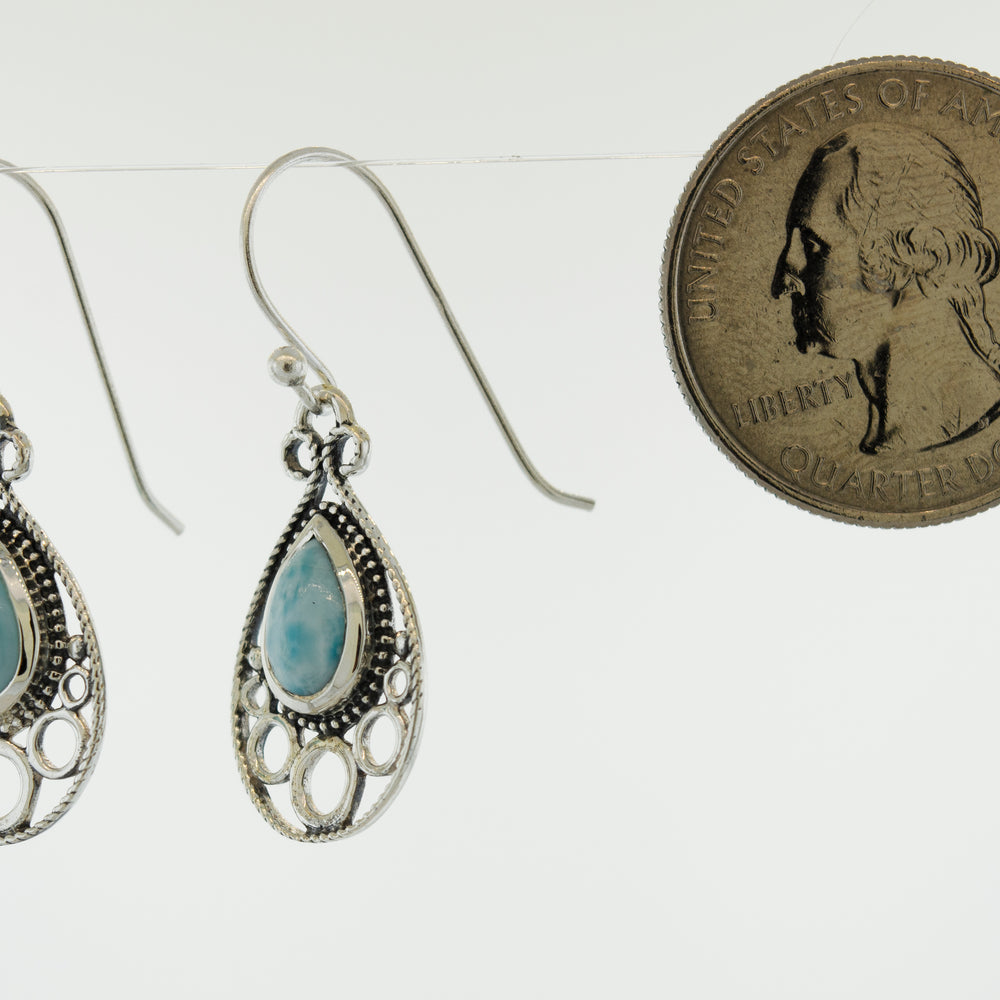 A pair of teardrop-shaped Super Silver earrings with a penny and a blue stone.
