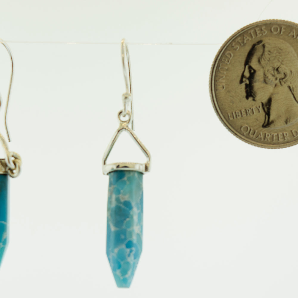 
                  
                    A pair of Obelisk Shape Raw Larimar Earrings from Super Silver with a blue jasper stone and a penny.
                  
                