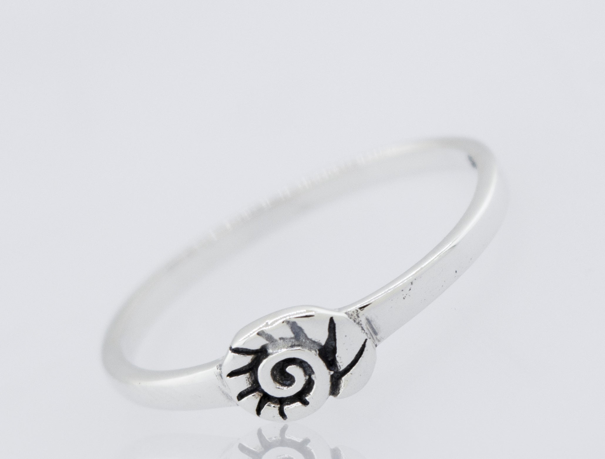 The Silver Nautilus Ring is a slim 925 Sterling Silver band with a small, stylized spiral and sunburst design, finished in high polish and displayed on a plain white background.
