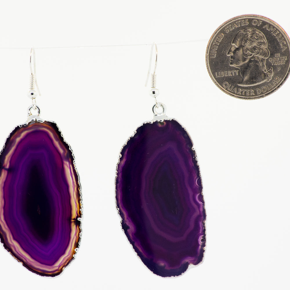 
                  
                    A purple slice of Super Silver dyed agate slice earrings, bordered by a silver-plated border, hanging from a string.
                  
                