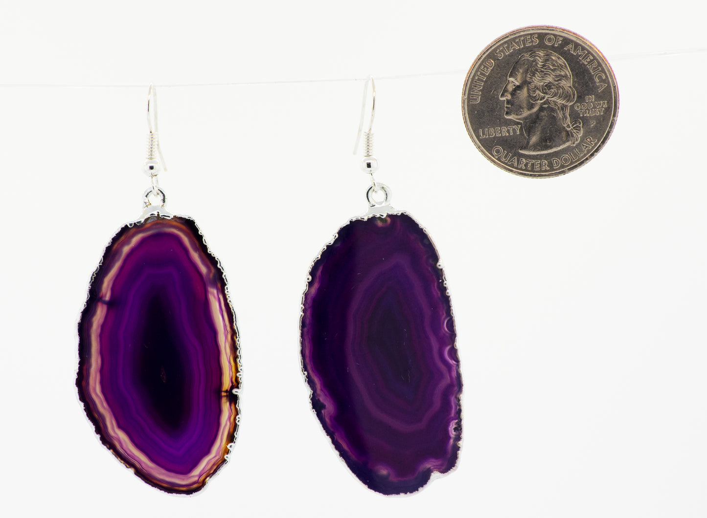 A purple slice of Super Silver dyed agate slice earrings, bordered by a silver-plated border, hanging from a string.