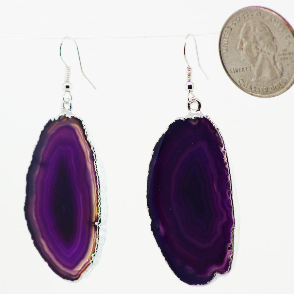 
                  
                    A purple Dyed Agate Slice Earrings hanging from a string with a Super Silver-plated border.
                  
                