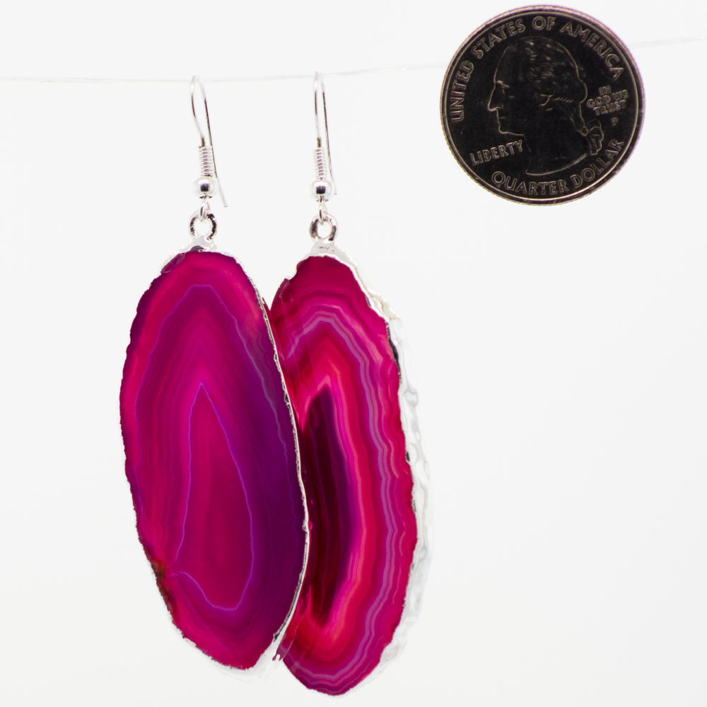 
                  
                    A pair of Super Silver Dyed Agate Slice earrings with a silver-plated border, hanging on a string.
                  
                