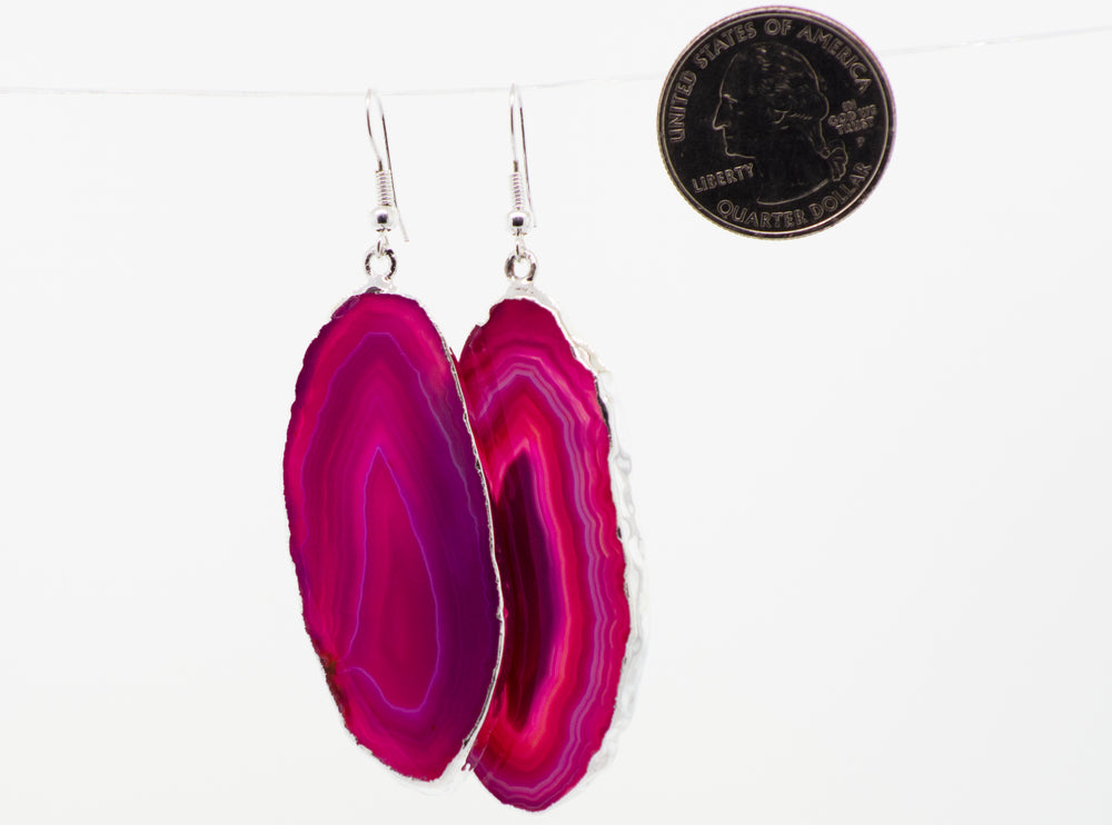 A pair of Super Silver Dyed Agate Slice earrings with a silver-plated border, hanging on a string.