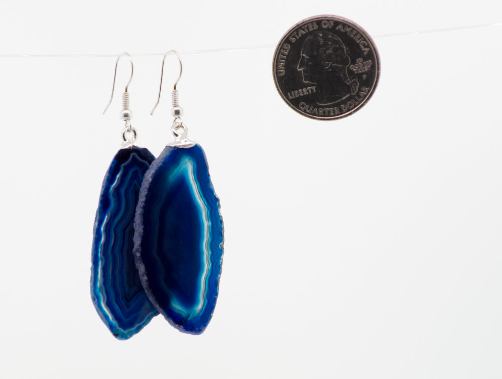 A pair of Super Silver Agate Slice Earrings hanging on a string.