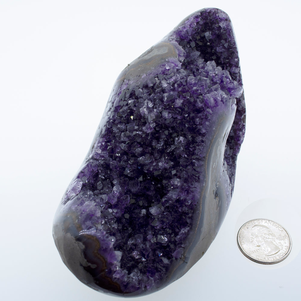 
                  
                    An Egg Shaped Amethyst Geode with a purple amethyst rock next to a dime.
                  
                