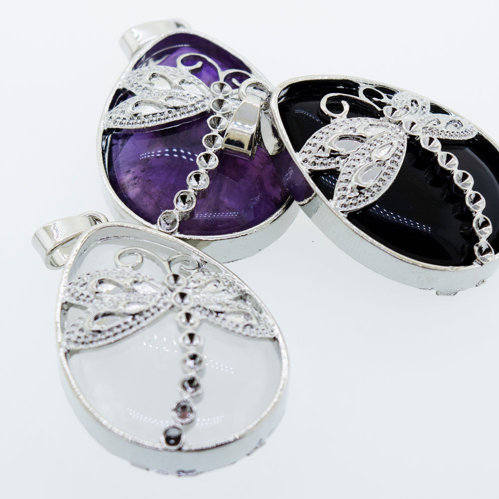 
                  
                    Three Silver plated Super Silver dragonfly pendants with Super Silver teardrop shaped stones on a white surface.
                  
                