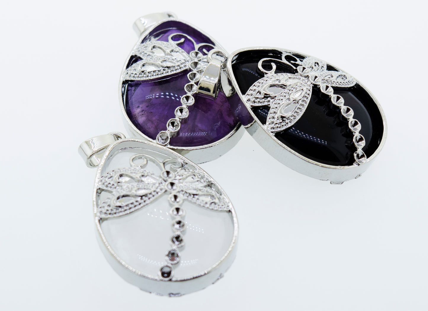 
                  
                    Three Silver plated Super Silver dragonfly pendants with Super Silver teardrop shaped stones on a white surface.
                  
                