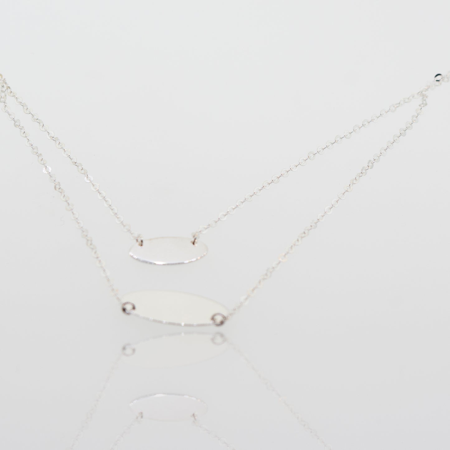 Two adjustable Super Silver sterling silver necklace with oval discs pendants on a white surface.
