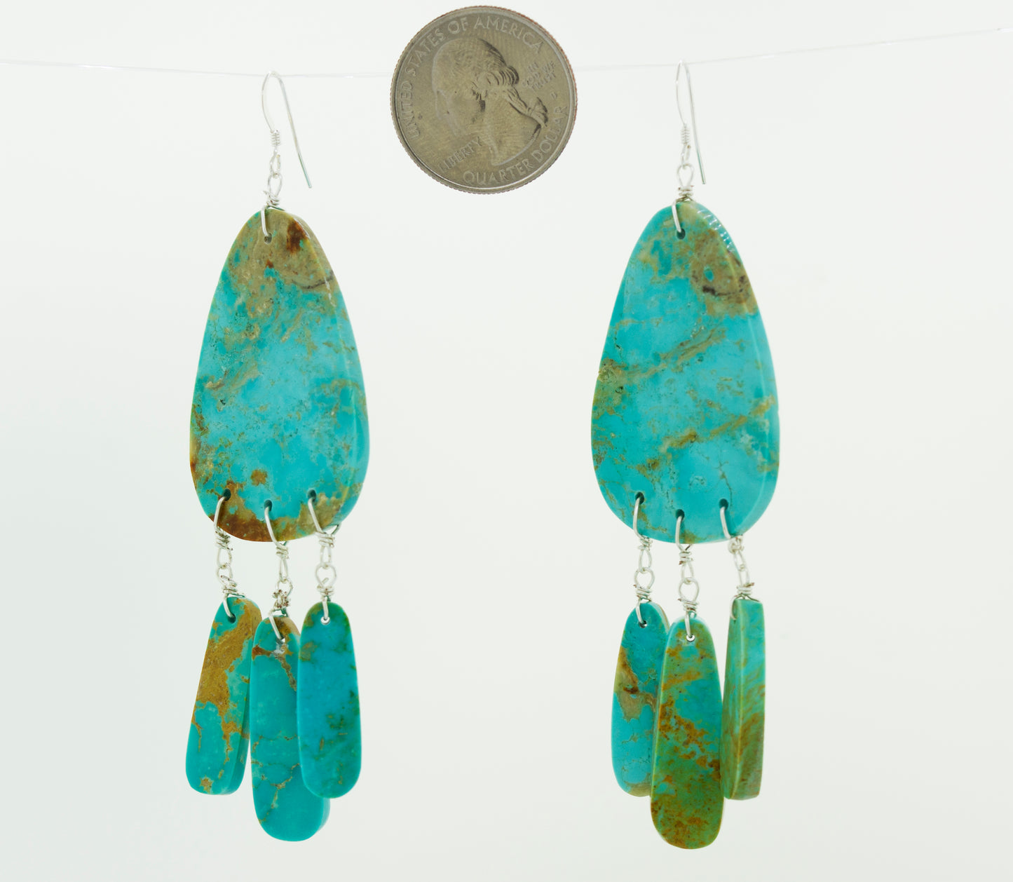
                  
                    A pair of Super Silver Native American Raw Turquoise Earrings elegantly dangle beside a coin.
                  
                