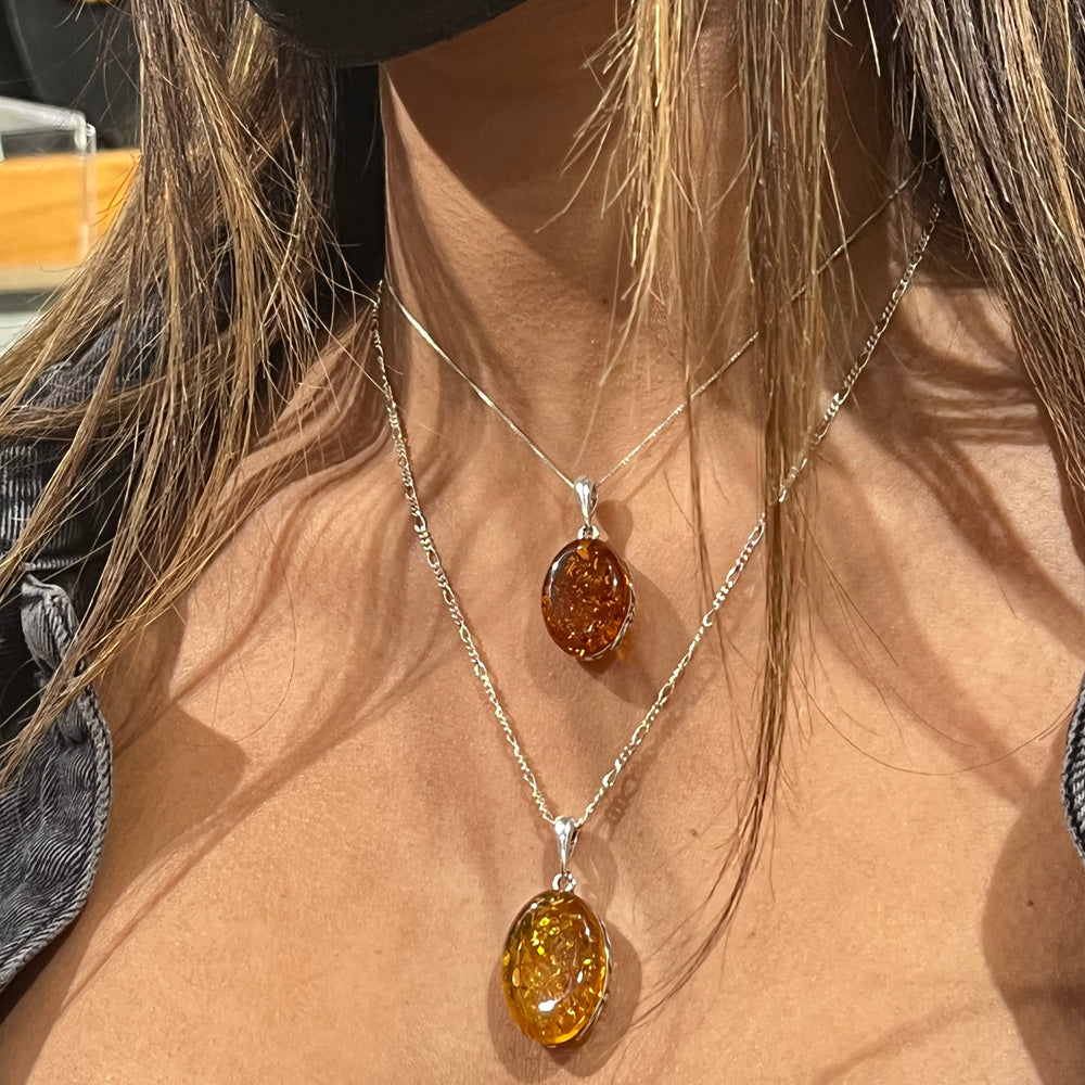 
                  
                    A woman wearing a mask and a Super Silver Cognac Amber Oval Pendant with Floral Border necklace.
                  
                
