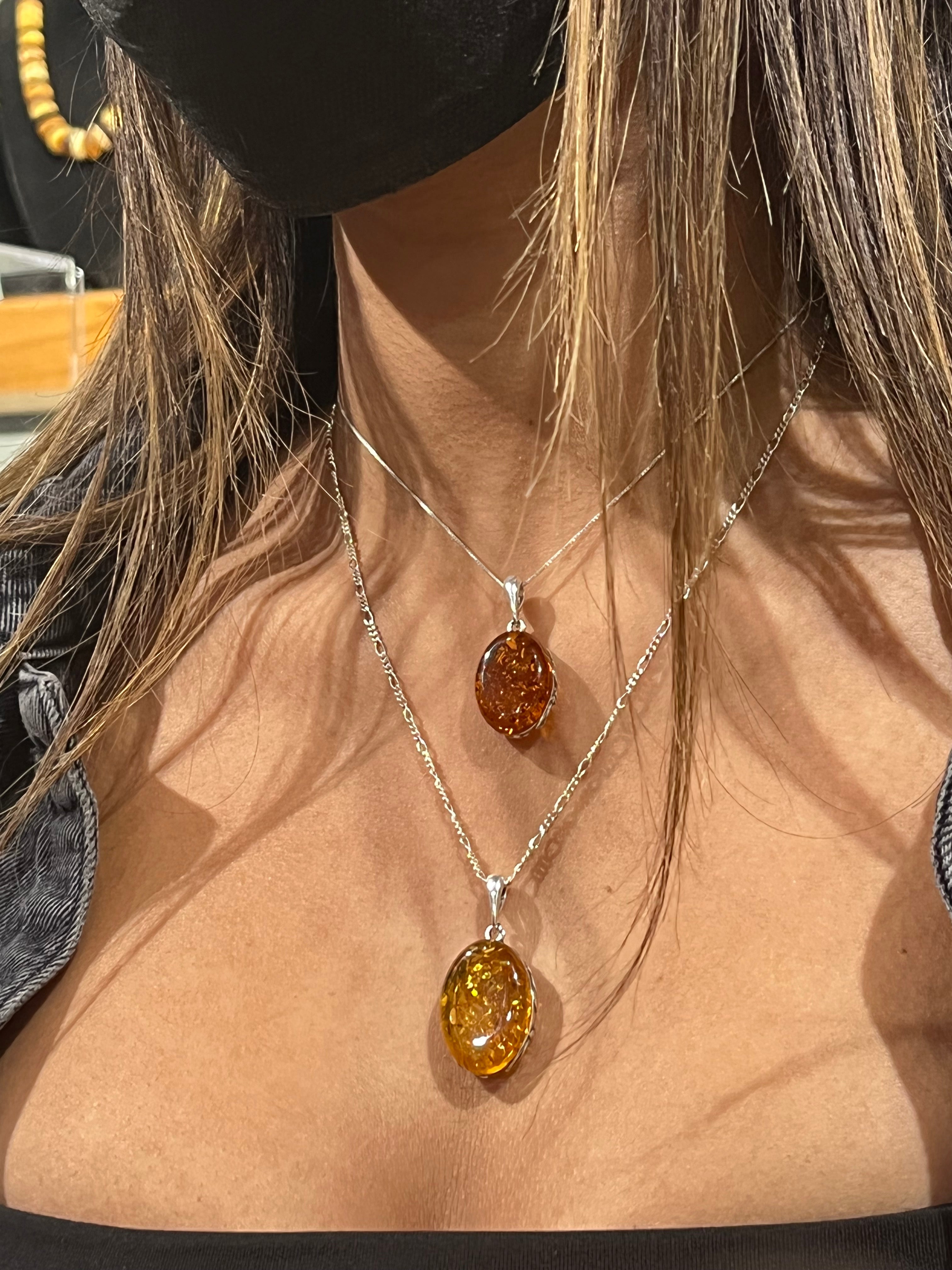 A woman wearing a mask and a Super Silver Cognac Amber Oval Pendant with Floral Border necklace.