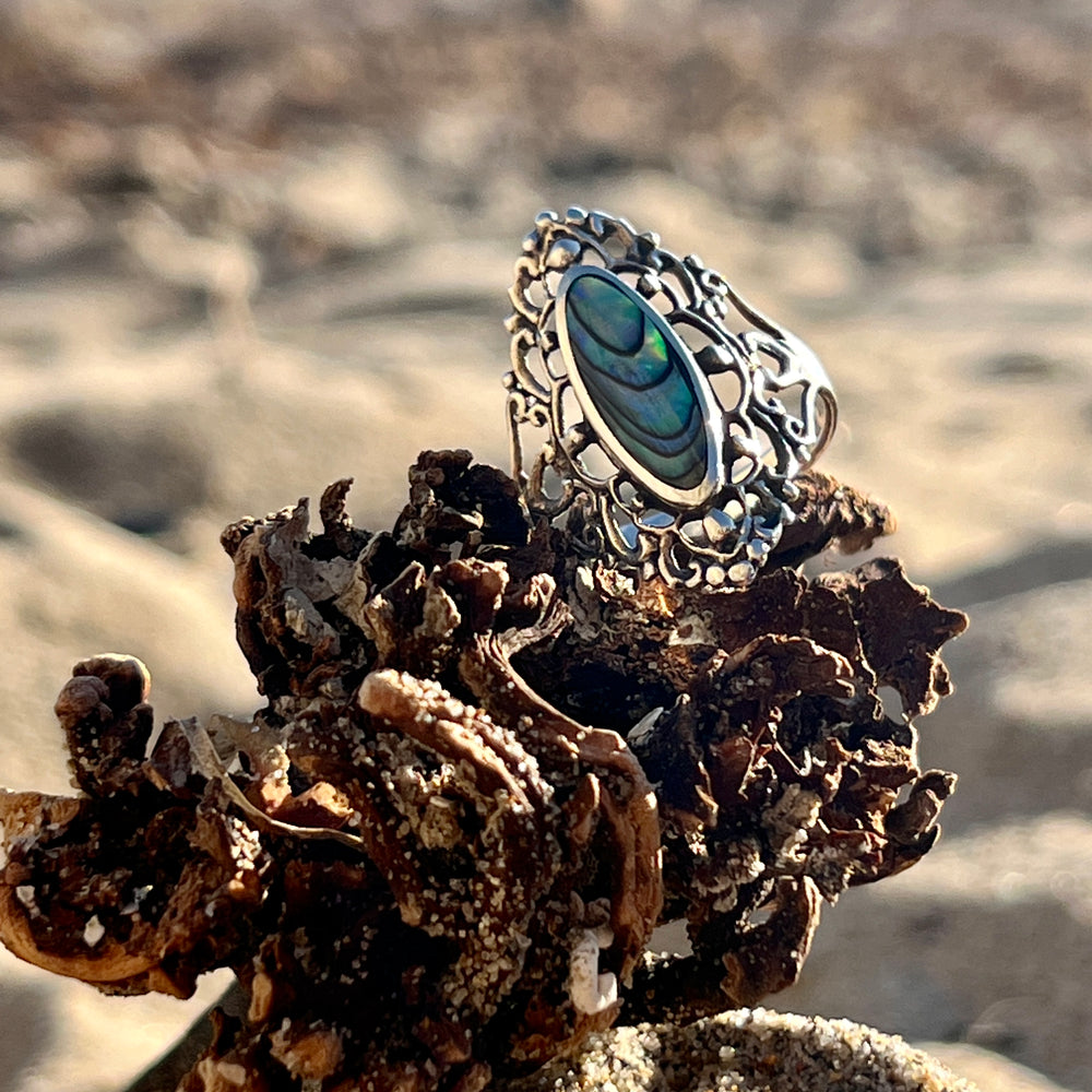 
                  
                    A Filigree Shield Ring with Inlaid Stones and an abalone shell inlaid on top of sand, made by Super Silver.
                  
                