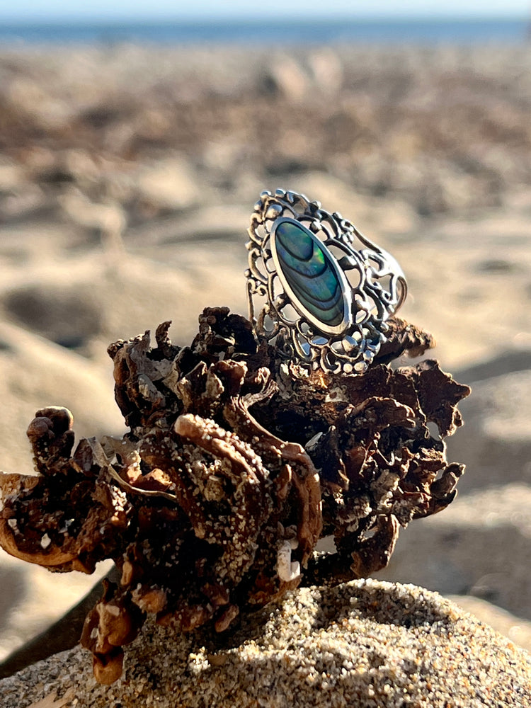 A Filigree Shield Ring with Inlaid Stones and an abalone shell inlaid on top of sand, made by Super Silver.
