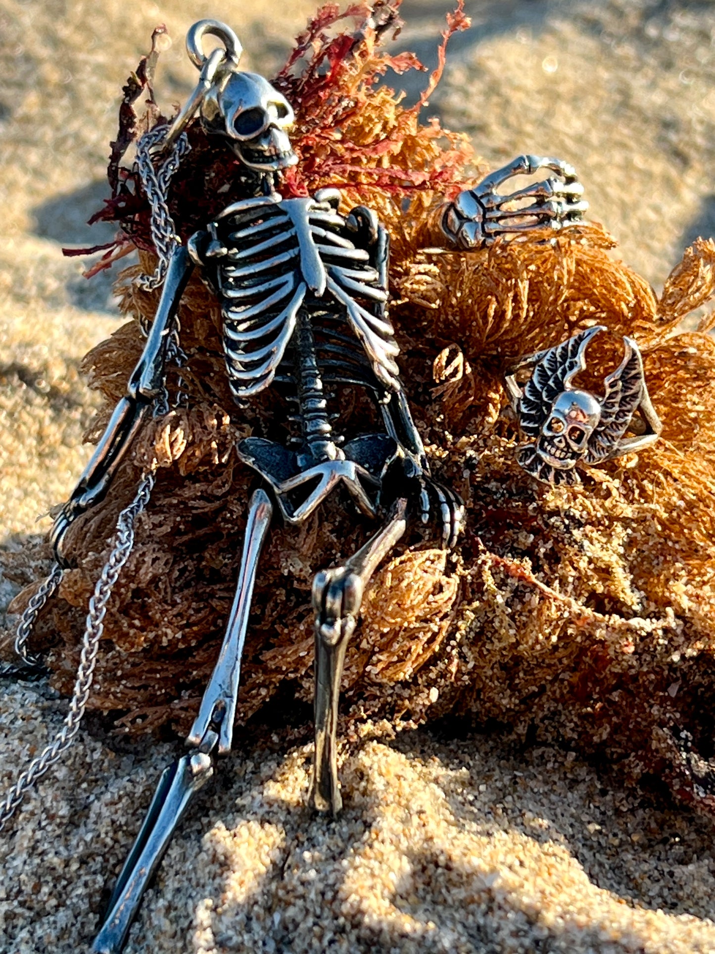 
                  
                    A gothic Skeleton Hand Ring perches on a rock in the sand.
                  
                