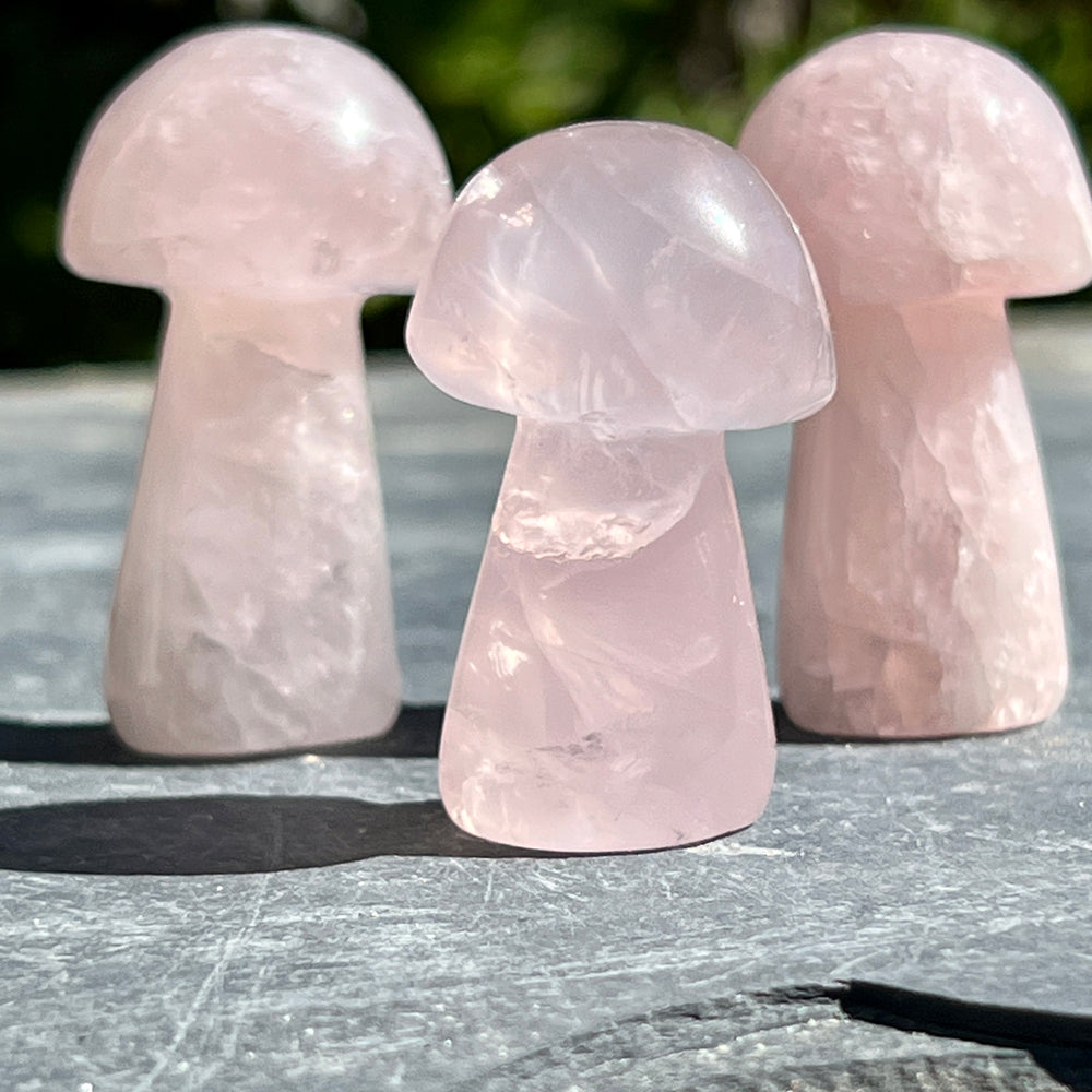 Three rose quartz mushrooms on a crystal-decorated stone table.