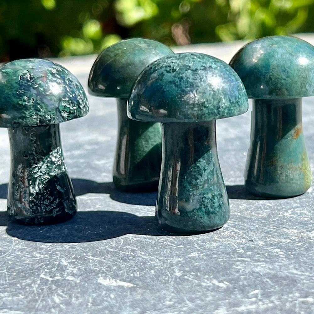 
                  
                    Three Moss Agate Mushroom stones on a table.
                  
                