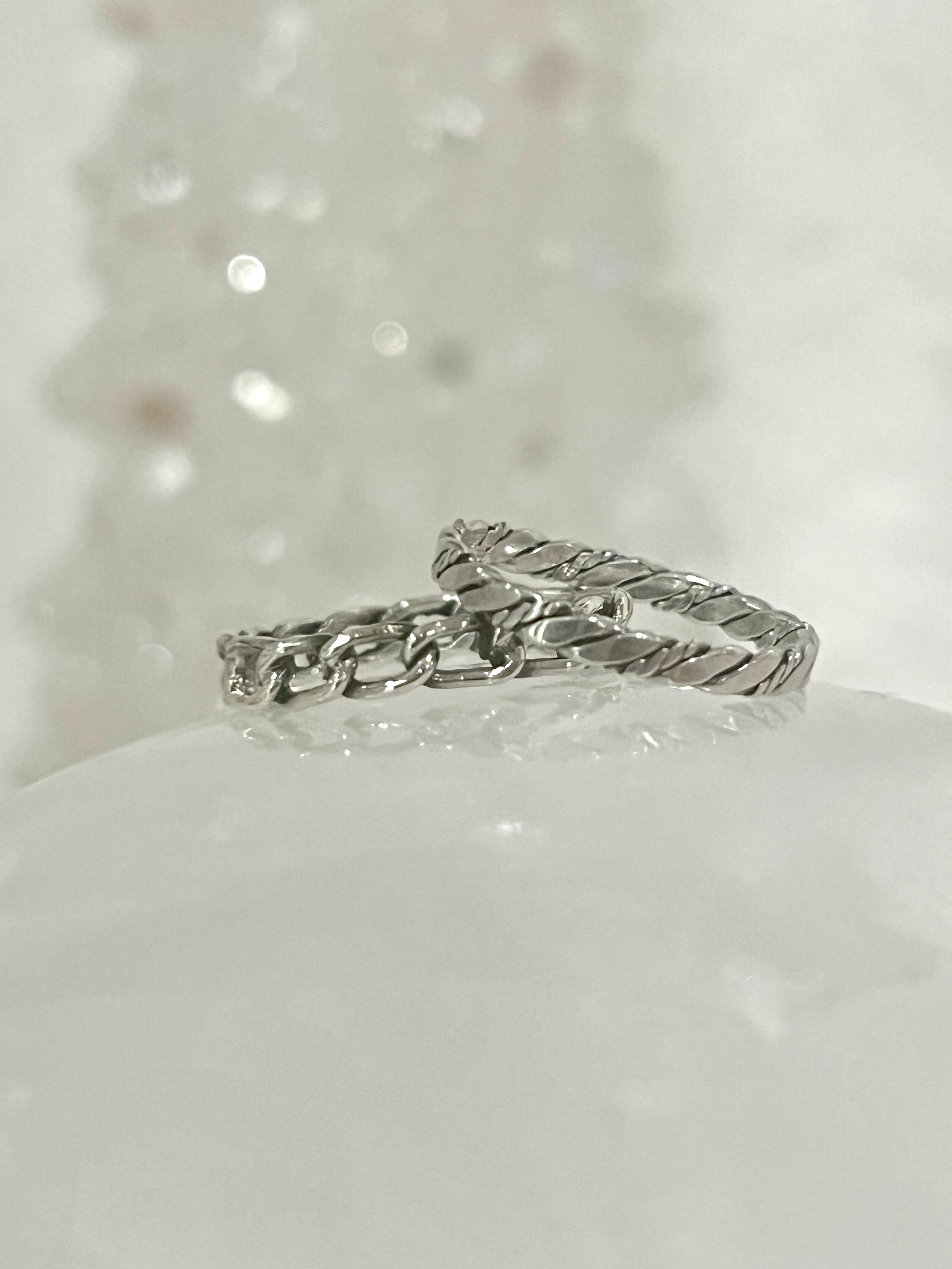 Two Dainty Twisted Rope Band Rings, with a rustic allure and vintage vibe, sitting on top of a piece of snow. (Super Silver)