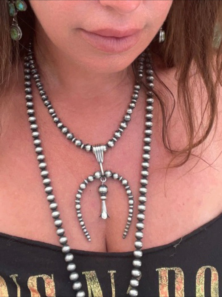 
                  
                    A woman wearing a Super Silver Handcrafted Naja Beaded Necklace, symbolizing protection and adorned with stunning Navajo pearls.
                  
                