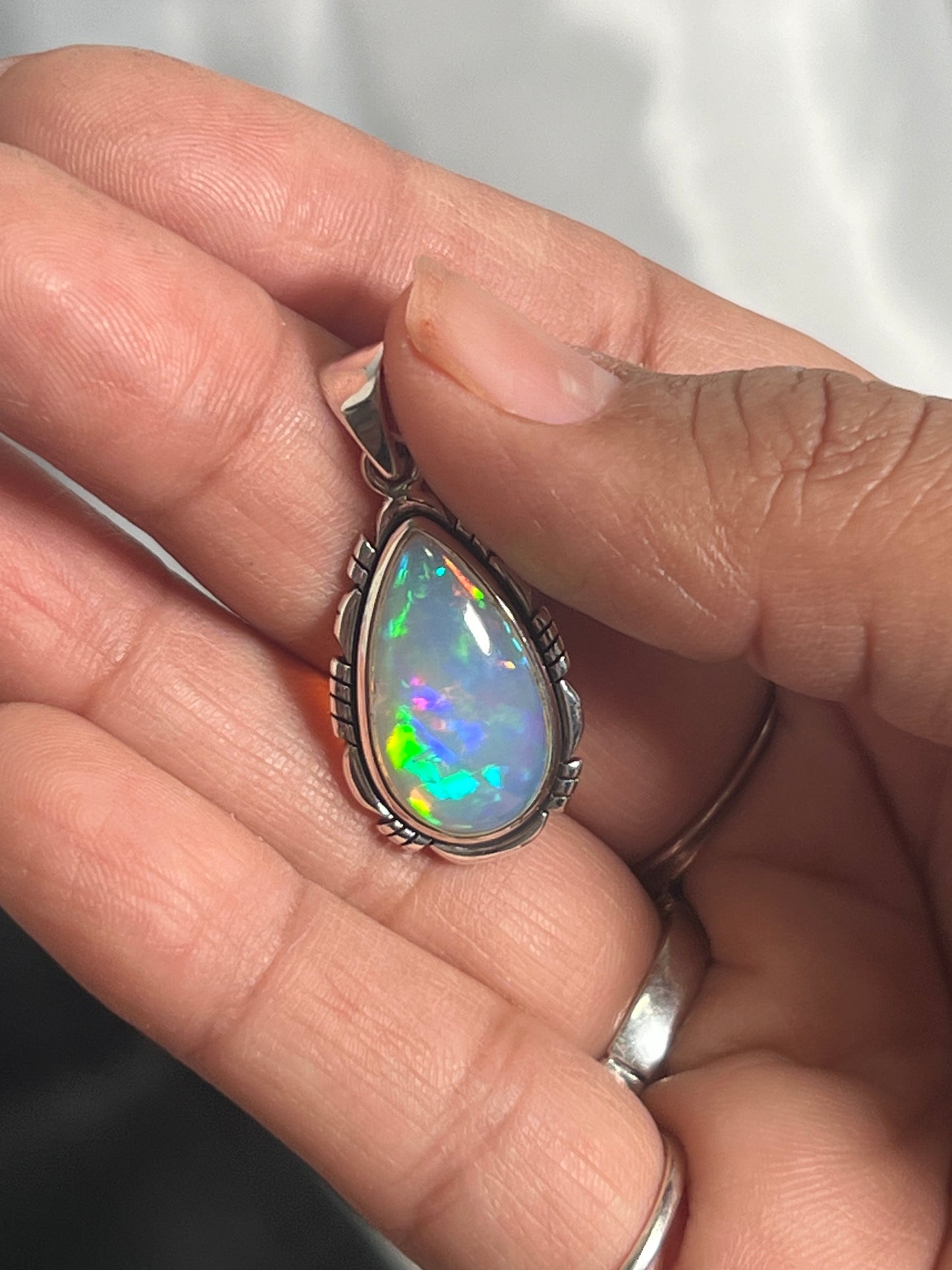 
                  
                    A person holding a Super Silver Ethiopian Opal Teardrop Shaped Pendant with Detailed Setting in their hand.
                  
                