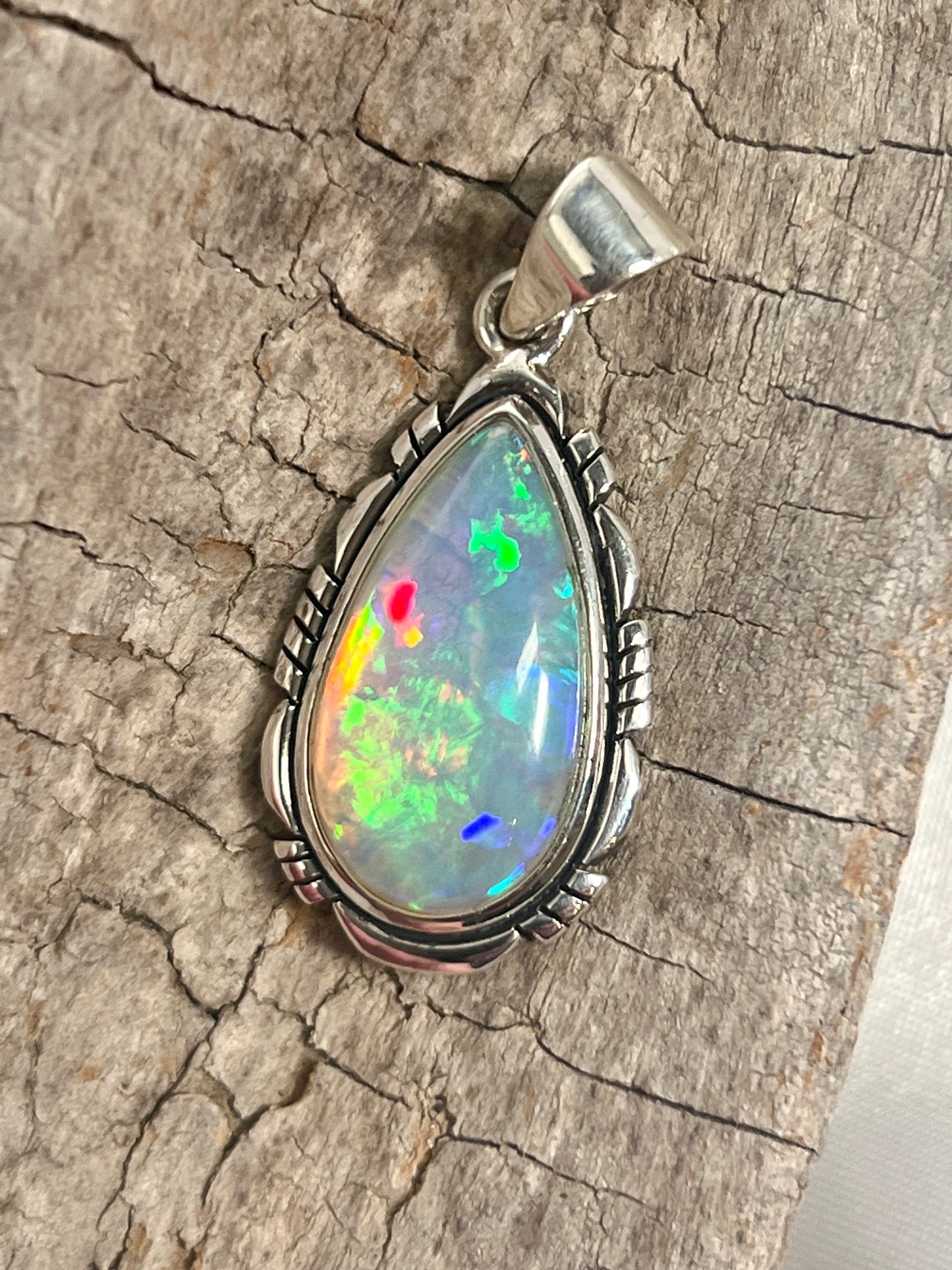 
                  
                    A stunning Super Silver Ethiopian Opal Teardrop Shaped Pendant with Detailed Setting, serving as a captivating statement piece, adorning a rustic piece of wood.
                  
                