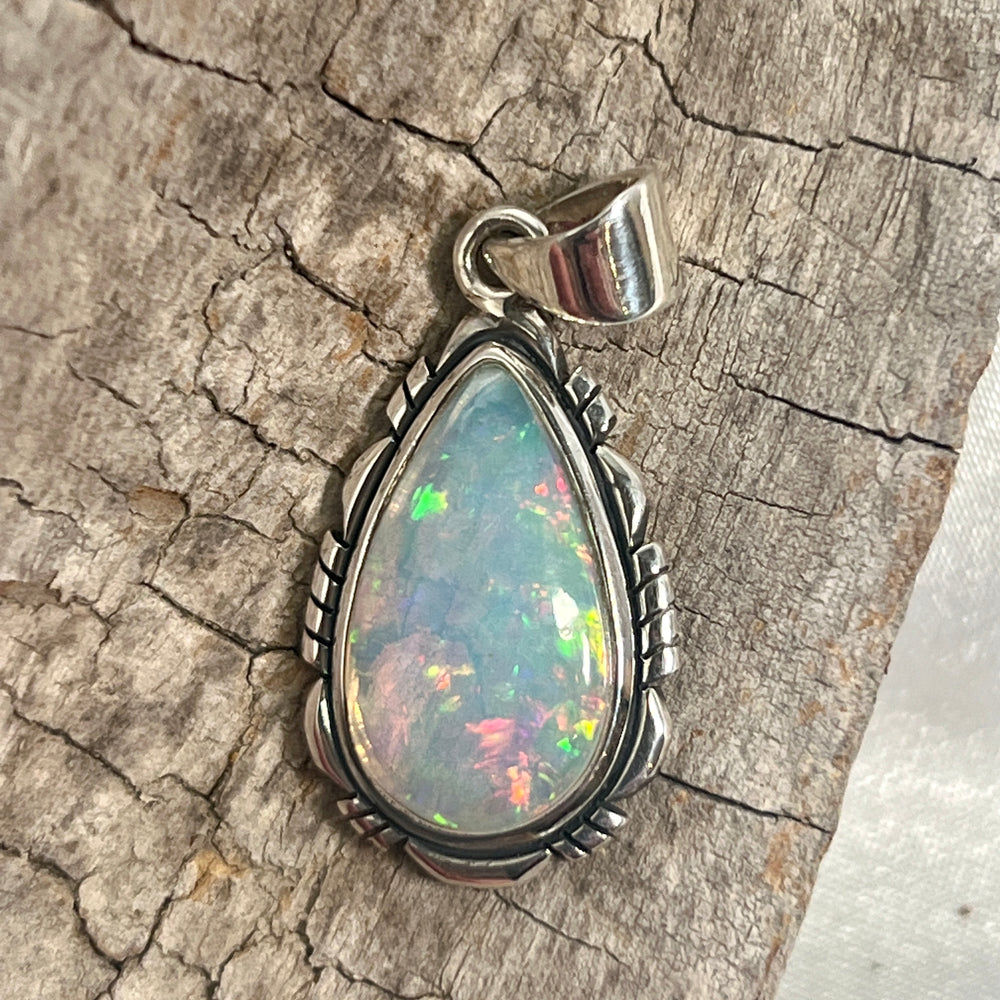 
                  
                    A stunning Ethiopian Opal Teardrop Shaped Pendant with Detailed Setting, truly a statement piece, delicately set on a piece of wood by Super Silver.
                  
                