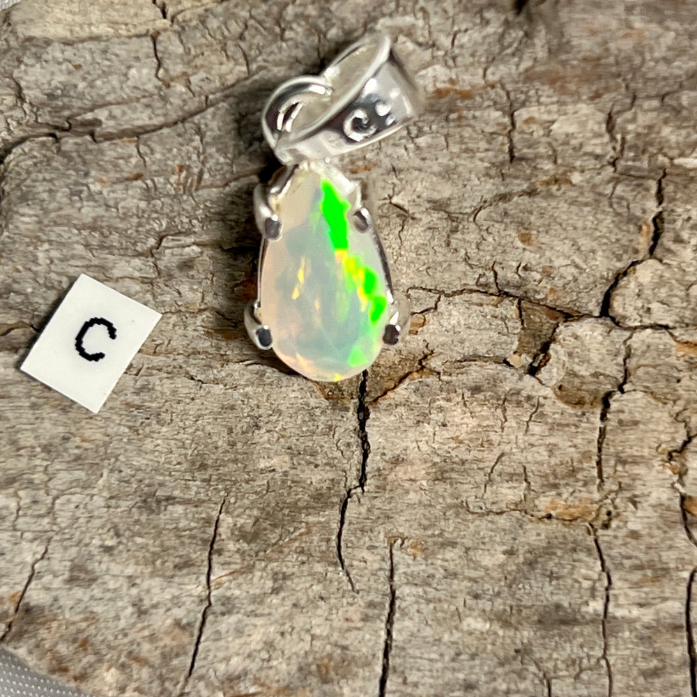 
                  
                    A Dainty Prong Set Facet Cut Teardrop Shaped Ethiopian Opal Pendant adorned with an exquisite Ethiopian Opal, gracefully suspended on a rustic piece of wood, by Super Silver.
                  
                