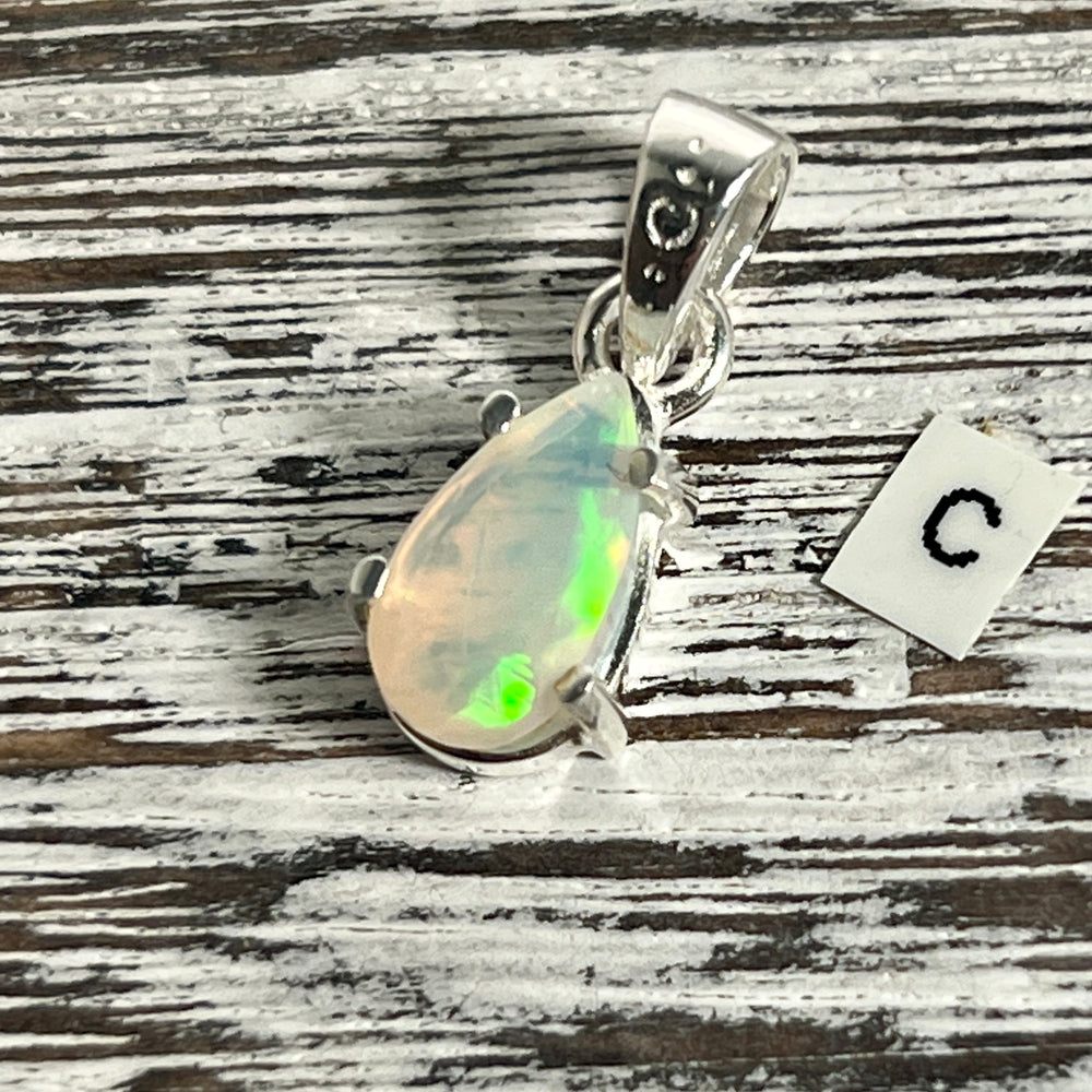 
                  
                    A Dainty Prong Set Facet Cut Teardrop Shaped Ethiopian Opal Pendant from Super Silver with the letter c on it.
                  
                