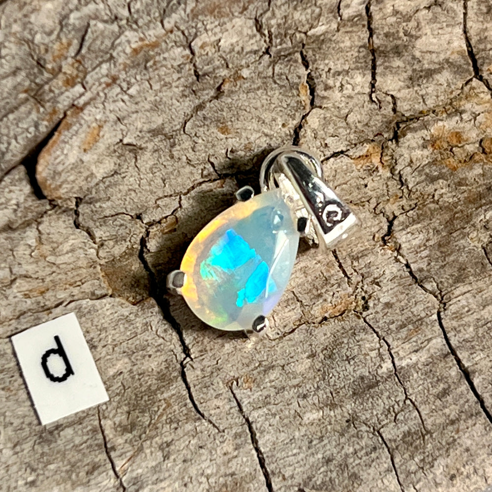
                  
                    A Super Silver Dainty Prong Set Facet Cut Teardrop Shaped Ethiopian Opal Pendant on a piece of wood.
                  
                