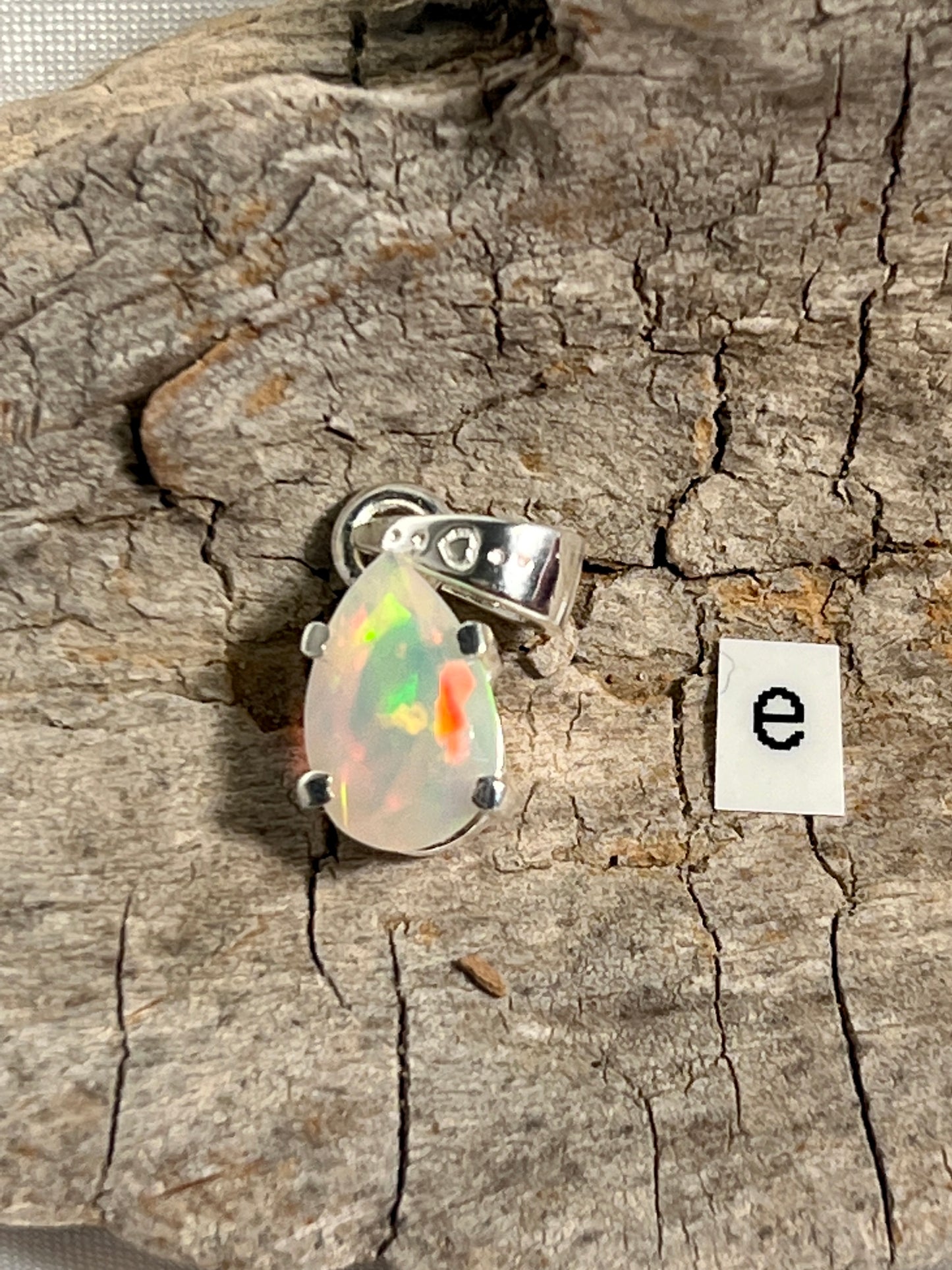
                  
                    A stunning Dainty Prong Set Facet Cut Teardrop Shaped Ethiopian Opal Pendant with the letter "e" delicately engraved on it, crafted in elegant sterling silver by Super Silver.
                  
                