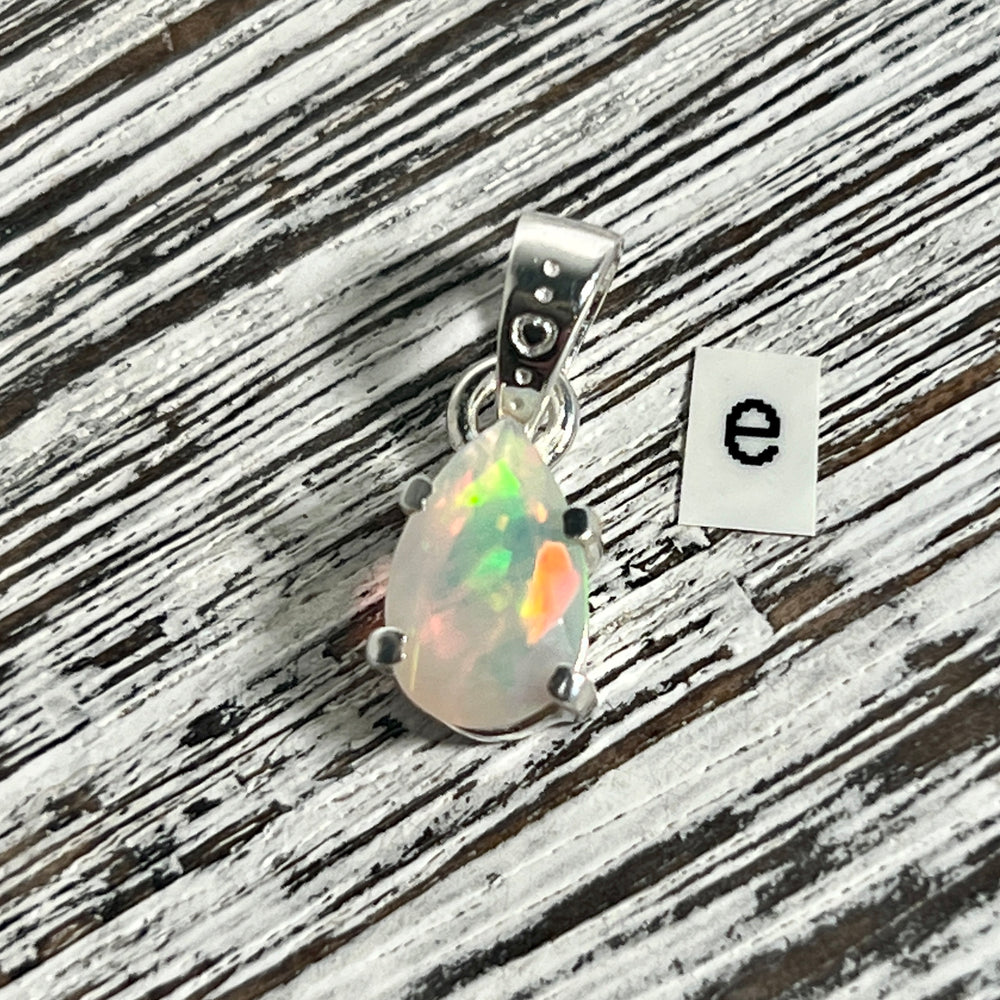 
                  
                    A Dainty Prong Set Facet Cut Teardrop Shaped Ethiopian Opal Pendant adorned with a stunning Ethiopian opal and featuring the letter e, produced by Super Silver.
                  
                