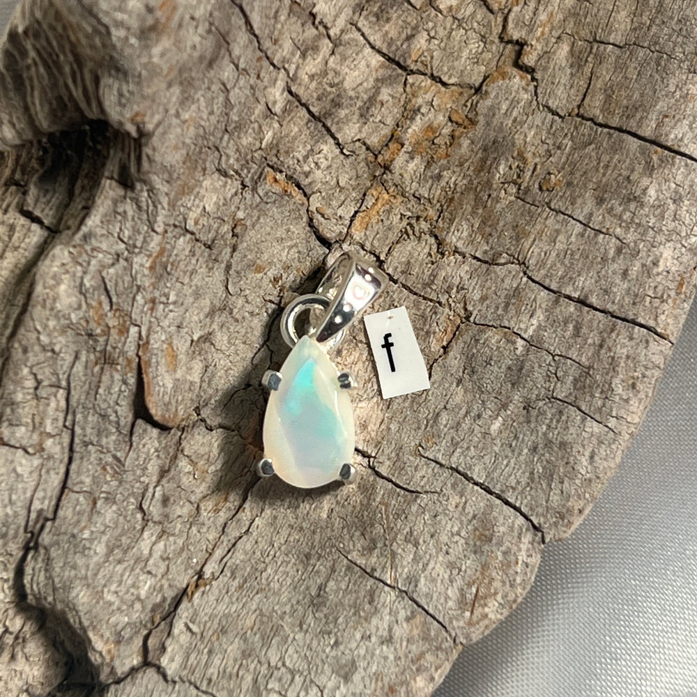 
                  
                    A stunning Dainty Prong Set Facet Cut Teardrop Shaped Ethiopian Opal Pendant on a piece of wood with a Super Silver accent.
                  
                