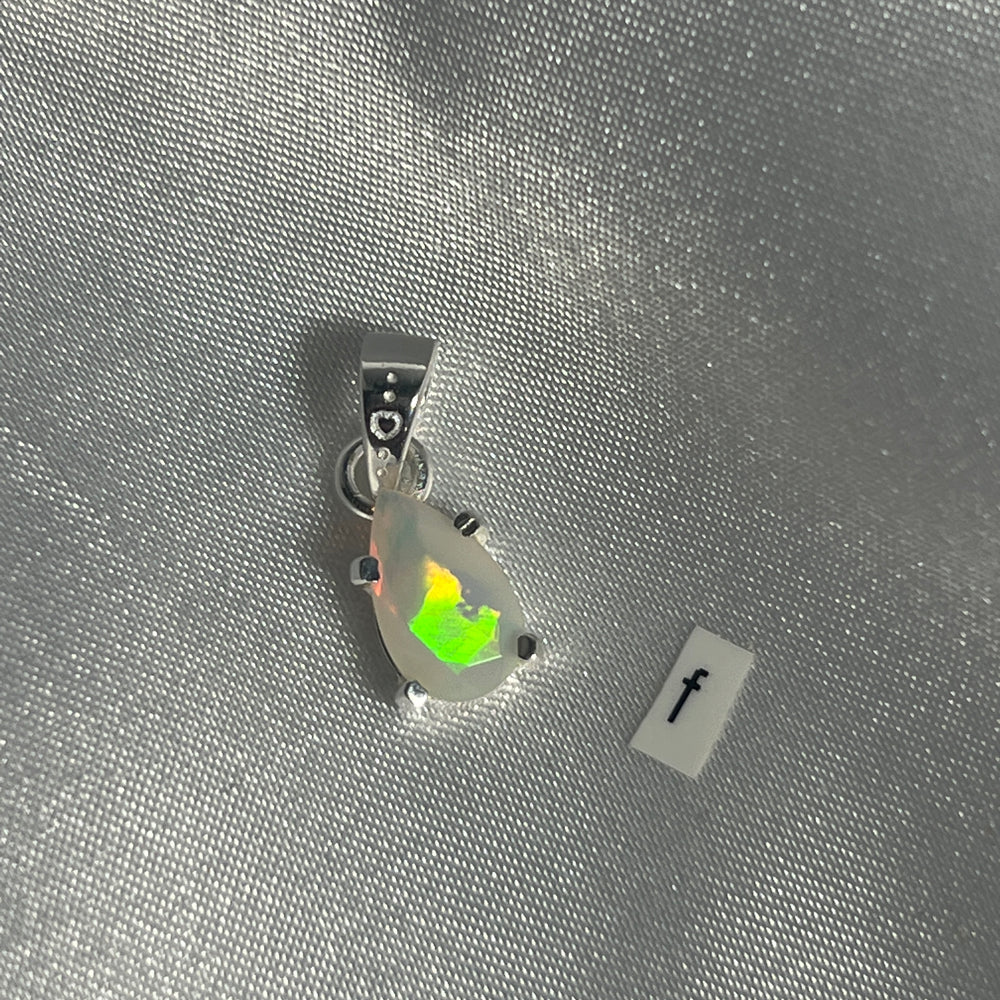 
                  
                    A Super Silver Dainty Prong Set Facet Cut Teardrop Shaped Ethiopian Opal pendant on a Sterling Silver surface.
                  
                